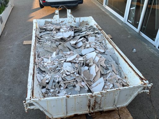benne gravats Bac à déchets rempli de débris en morceaux, situé sur un sol bétonné.