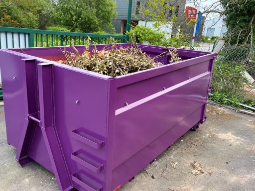 Benne Végétaux Container de déchets de couleur violette rempli de débris végétaux.